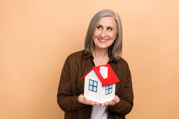 Sticker - Portrait of charming minded lady hold little house look empty space brainstorming isolated on beige color background