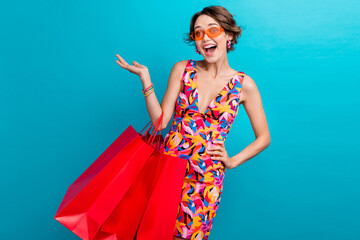 Wall Mural - Photo of funky woman with bob hair dressed colorful clothes hold new outfit palm demonstrate empty space isolated on blue color background