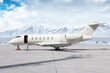 Modern white private jet with an opened gangway door at the winter airport apron on the background of high scenic snow capped mountains