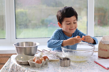 Child broke fresh egg. Child hand crack egg for cooking, baking cake, waffles at home in the kitchen. Fresh free range eggs in a glass bowl. Close up photo family lifestyle.