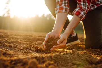 Close-up of a farmer's hands taking black soil from the field. Men's hands move the soil with their hands, checking its quality. Ecology concept.