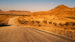 Warm sunset light bathing the Namib Desert traversed by a gravel road, east of Khorixas, Kunene, Namibia