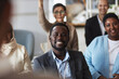 © Seventyfour - Young smiling African American businessman in formalwear listening to speaker at seminar while sitting between female employees