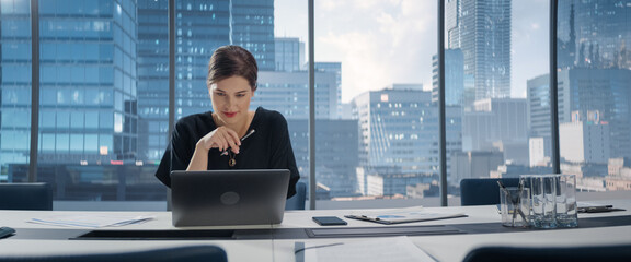 Poster - Portrait of Young Successful Caucasian Businesswoman Sitting at Desk Working on Laptop Computer in City Office. Female Manager Plan Investment Strategy for e-Commerce Project.