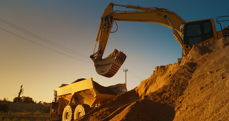 Wall Mural - Construction Site On Sunny Evening: Industrial Excavator Loading Sand Into A Truck. The Process Of Building New Apartment Block. Workers Operating Heavy Machinery To Complete New Real Estate Project.