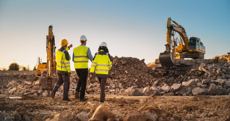 construction site with excavators on sunny day: diverse team of male and female specialists walking 