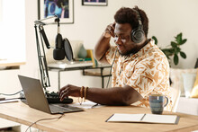 Young African American male blogger or radio presenter adjusting soundboard before recording new podcast by workplace