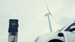 © Summit Art Creations - Progressive future energy infrastructure concept of electric vehicle being charged at charging station powered by green and renewable energy from a wind turbine in order to preserve the environment.