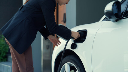 Wall Mural - A woman unplugs the electric vehicle's charger at his residence. Concept of the use of electric vehicles in a progressive lifestyle contributes to a clean and healthy environment.