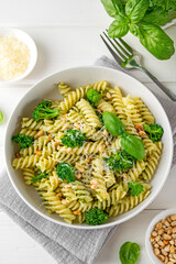 Wall Mural - Vegetarian pasta with pesto sauce, broccoli, parmesan cheese and pine nuts on a white wooden background. Healthy food.