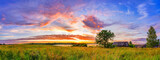 Fototapeta Miasta - Panoramic view on sunset over old wooden hut and lonely tree in countryside