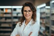 © Georgii - Portrait of a charming young Caucasian female pharmacist wearing glasses with arms folded on her chest among shelves with medicines in a pharmacy. Experienced confident professional in the workplace.