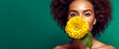 Beautiful poc young woman with curly black hair holding yellow flower. Green background. Natural cosmetics fashion concept. Banner with copy space