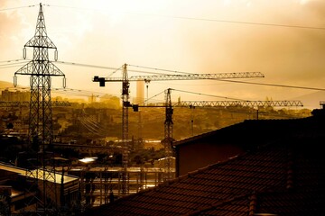 Poster - a view over a city with construction cranes at sunset time