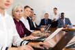 © JackF - Portrait of elegant elderly white gray-haired female manager attending business meeting in conference room and watching colleague's presentation together with coworkers