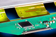 Closeup a printed circuit board with microchips, capacitors or resistors. Black micro chips and small surface mounted electronic components on green PCB with plastic flexible parts inside a LCD panel.