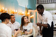 Positive elegant couple talking with polite african american waiter while dining in cozy restaurant
