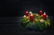Light in the dark on second advent, natural green wreath with red candles, two are burning, Christmas decoration and cookies, dark wooden background, copy space