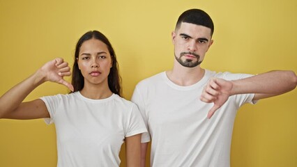 Wall Mural - Uncool vibes – beautiful couple together, seriously thumbs-down, against a strikingly yellow isolated wall