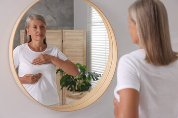 Poster - Beautiful senior woman doing breast self-examination near mirror in bathroom