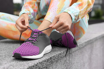 Poster - Woman in gym clothes tying shoelace of sneakers on street, closeup