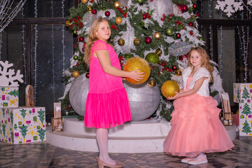 Wall Mural - Beautiful elegant girls near the Christmas tree in the New Year. Holiday. New Year. Children are models. Two sisters.