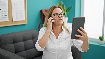 Canvas Print - Middle age hispanic woman business worker talking on smartphone using touchpad at the office