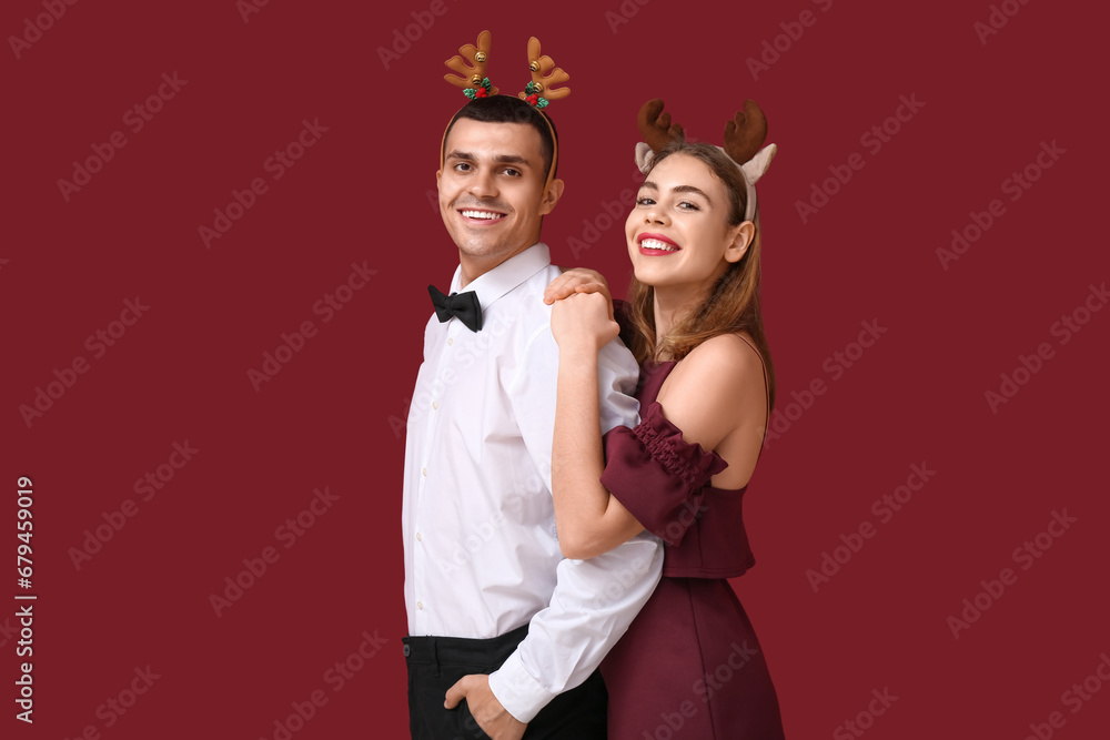 Beautiful young couple in reindeer horns on red background