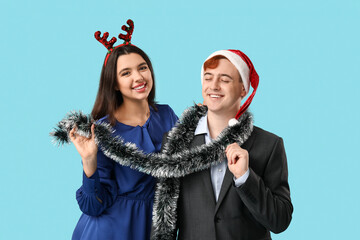 Sticker - Happy young couple with Christmas tinsel on blue background