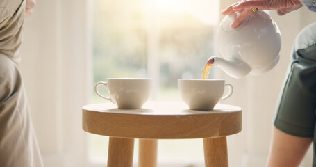 Sticker - Pot, pour and hands with tea cup in morning, home and closeup on drink, steam and table. Hot, beverage and person with hospitality, service and drinking in the afternoon with friends in living room