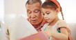 Grandparent, kid and reading book with smile, home and child development, grandchild and couch. Man, lounge or bonding together for relationship, family and retired with girl, house and happy