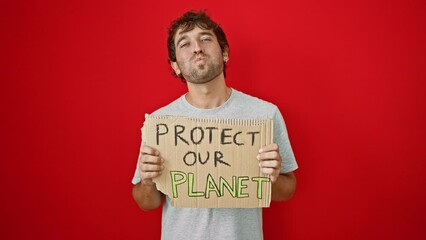 Canvas Print - Hilarious expression of a young blond guy visage inflated with air, puffing cheeks whilst holding a 'protect our planet' banner on an isolated red background