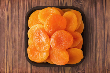 Wall Mural - dried apricots in square plate on wooden table background. vegetarian organic food for healthy diet.