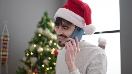 Sticker - Young hispanic man speaking on the phone by christmas tree at home