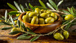 Closeup of an old olive wood bowl, full of fresh green olives wet with dew, on a wooden table with olive branches.