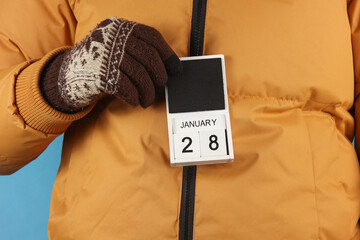 Man in yellow winter down jacket and gloves holding block calendar with date january 28 on blue background