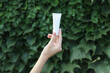 © splitov27 - Hand holding white cream tube on green leaves wall background
