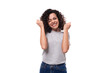 kind slender young caucasian woman with careless black curly hair is dressed in a gray t-shirt on a white background