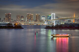 Fototapeta  - Japan Travel Destinations. Closeup View of Rainbow Bridge in Odaiba Island in Tokyo At Twilight with Tourist Boat and Line of Skyscrapers.