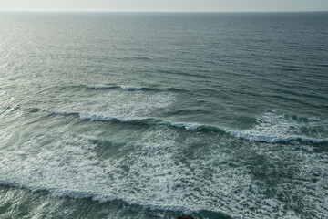 Wall Mural - ocean foamy waves approaching rocky shore. top view.