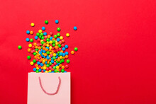 Shopping Paper Gift Bag In Corner Full Of Assorted Traditional Candies Falling Out On Colored Background With Copy Space. Happy Holidays Sale Concept