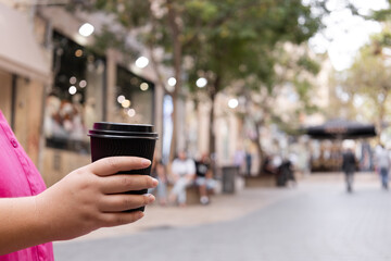 a close-up of a woman holding a black plastic coffee cup in hand. coffee break in the city center wi