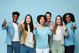 Fototapeta  - Group of young people with approving expression looking at camera showing success and like gesture on blue background. Diverse happy multiracial people holding raised thumbs ups.