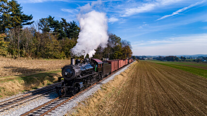 Canvas Print - An Aerial View of an Antique Steam Freight Passenger Train Blowing Smoke as it Slowly Travels on an Autumn Day
