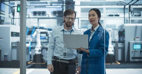 Fototapete - Industrial Engineers Working at a Technology Factory. Caucasian Man and Asian Female Using Laptop Computer and Having a Conversation. Footage with a Portrait of a Couple of Employees at a Plant