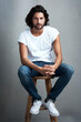 © Jadon Bester/peopleimages.com - Fashion, handsome and portrait of man in studio on a stool with casual, cool and stylish outfit. Confidence, serious and young male model from Mexico with trendy style on chair by gray background.