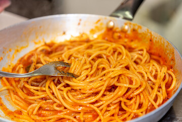 Wall Mural - Spaghetti pasta with tomato sauce cooking in pan with fork, selective fire close up