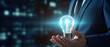 © Synthetica - Businessman on blurred background holding a glowing light bulb in his hand.