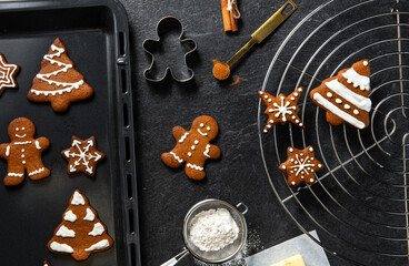 Wall Mural - christmas, food cooking and winter holidays concept - close up of iced gingerbread cookies, molds, flour and oven tray on black table top at kitchen