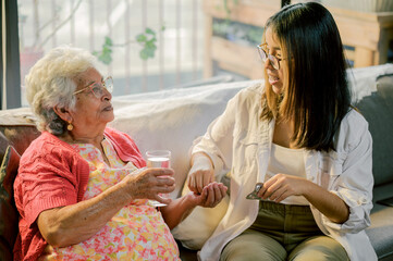 Granddaughter takes care of her grandmother, gives her pills and a glass of water.